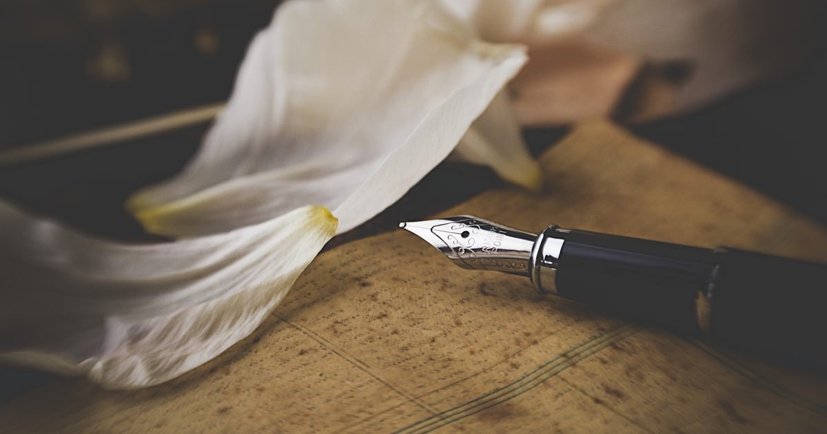Caneta-tinteiro sobre papel antigo, ao lado de uma flor branca