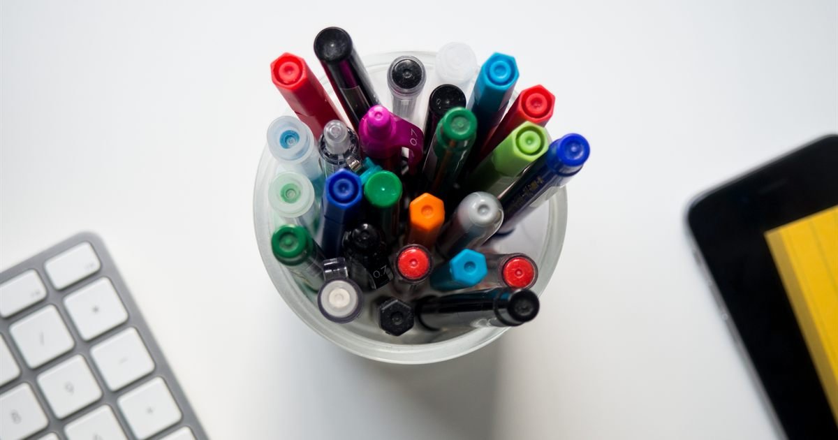 Copo com canetas coloridas ao lado de um teclado