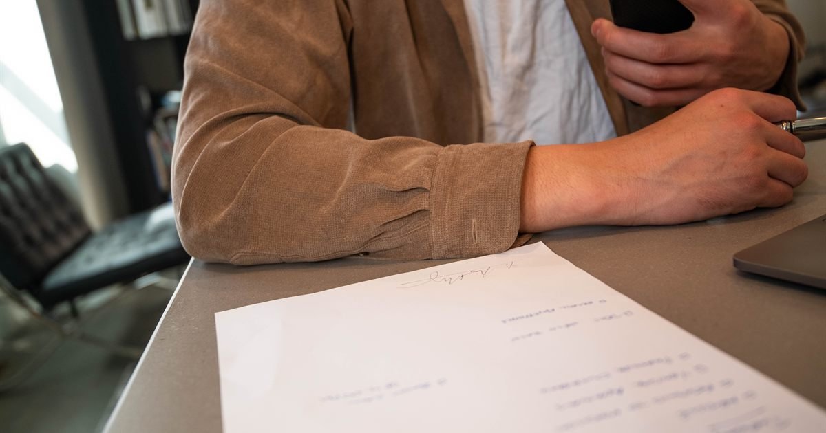 Pessoa assinando papéis sobre uma mesa, sem o rosto visível