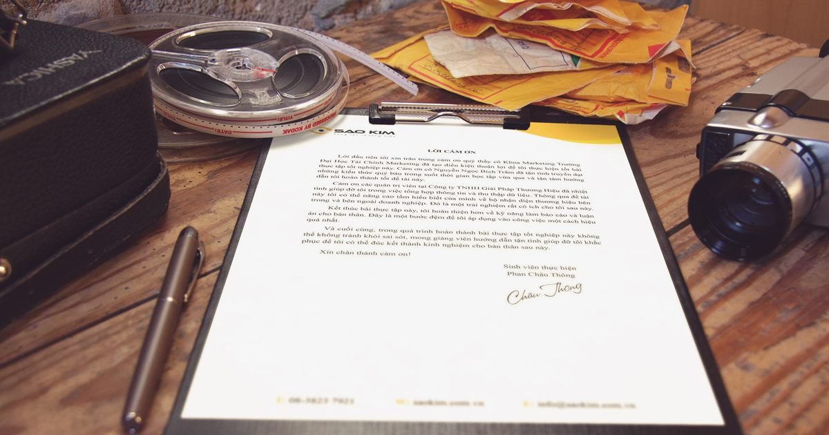 Carta presa em prancheta sobre mesa de madeira, com câmera e envelopes