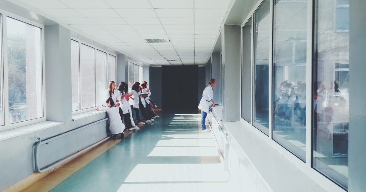 Corredor de hospital amplo e iluminado, com profissionais de saúde ao fundo