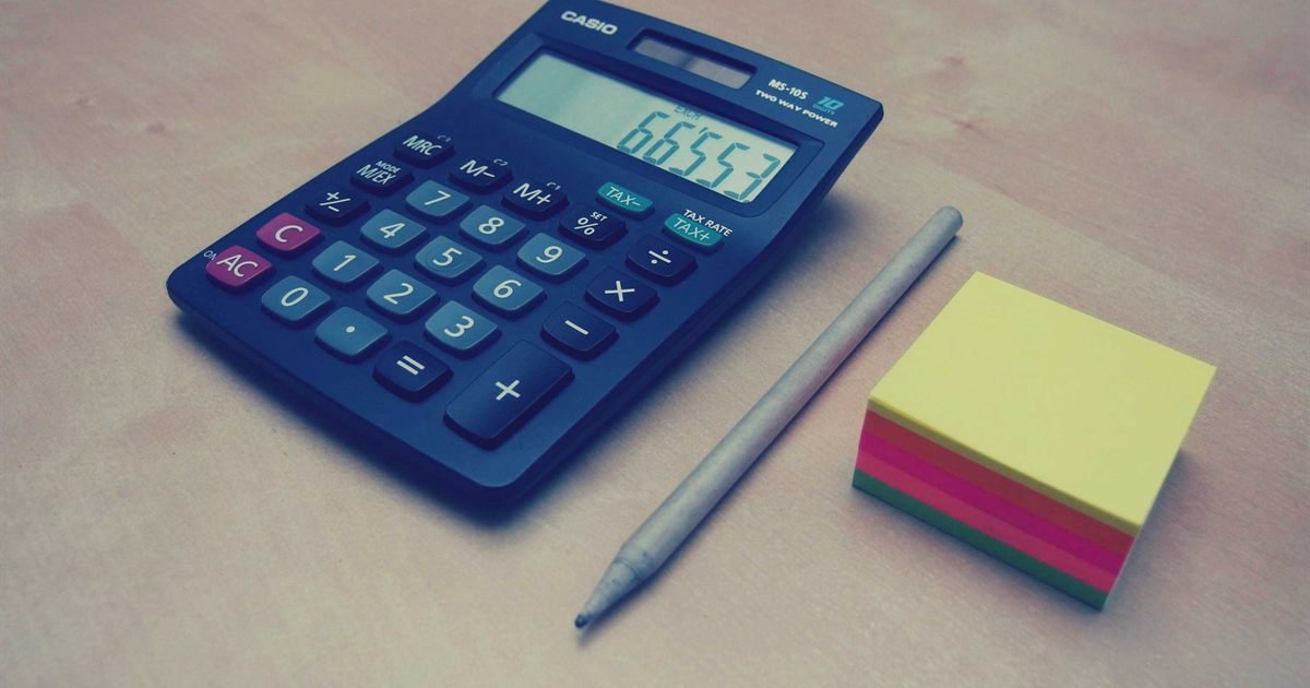 Calculadora azul, lápis e bloco de notas sobre uma mesa