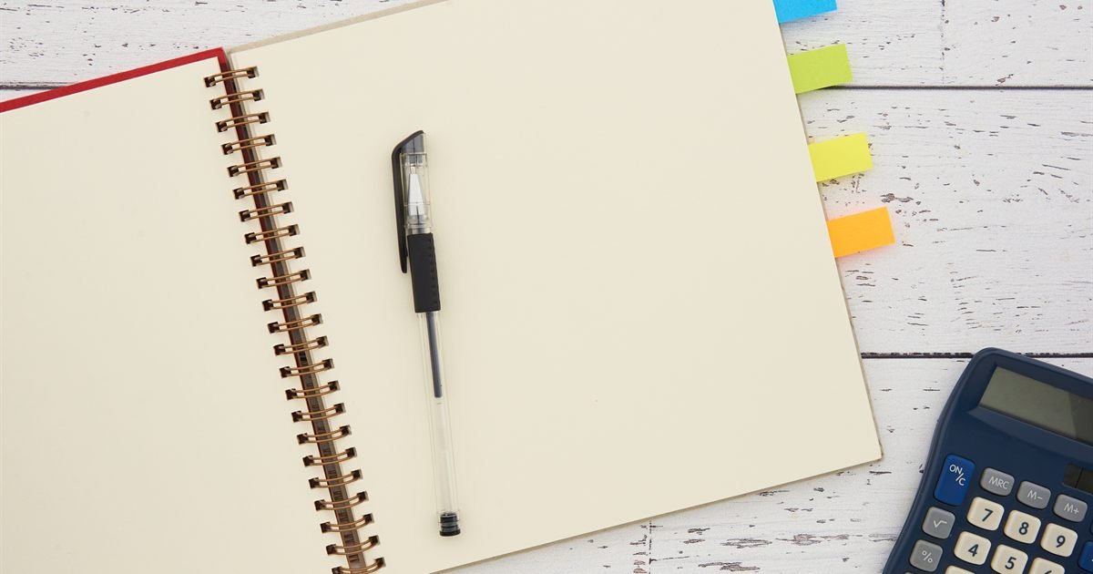 Caderno aberto com caneta e uma calculadora ao lado
