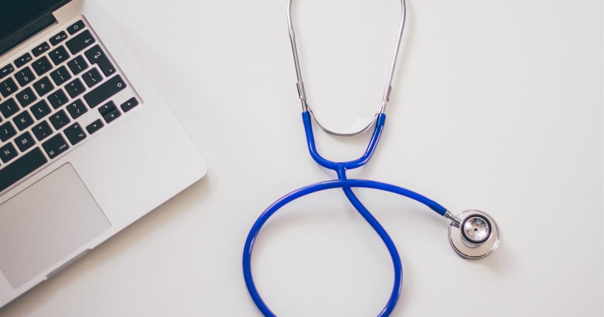 Estetoscópio azul ao lado de um notebook sobre mesa branca